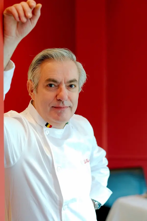 Pascal Romano en veste de cuisinier, devant le mur rouge de la salle
