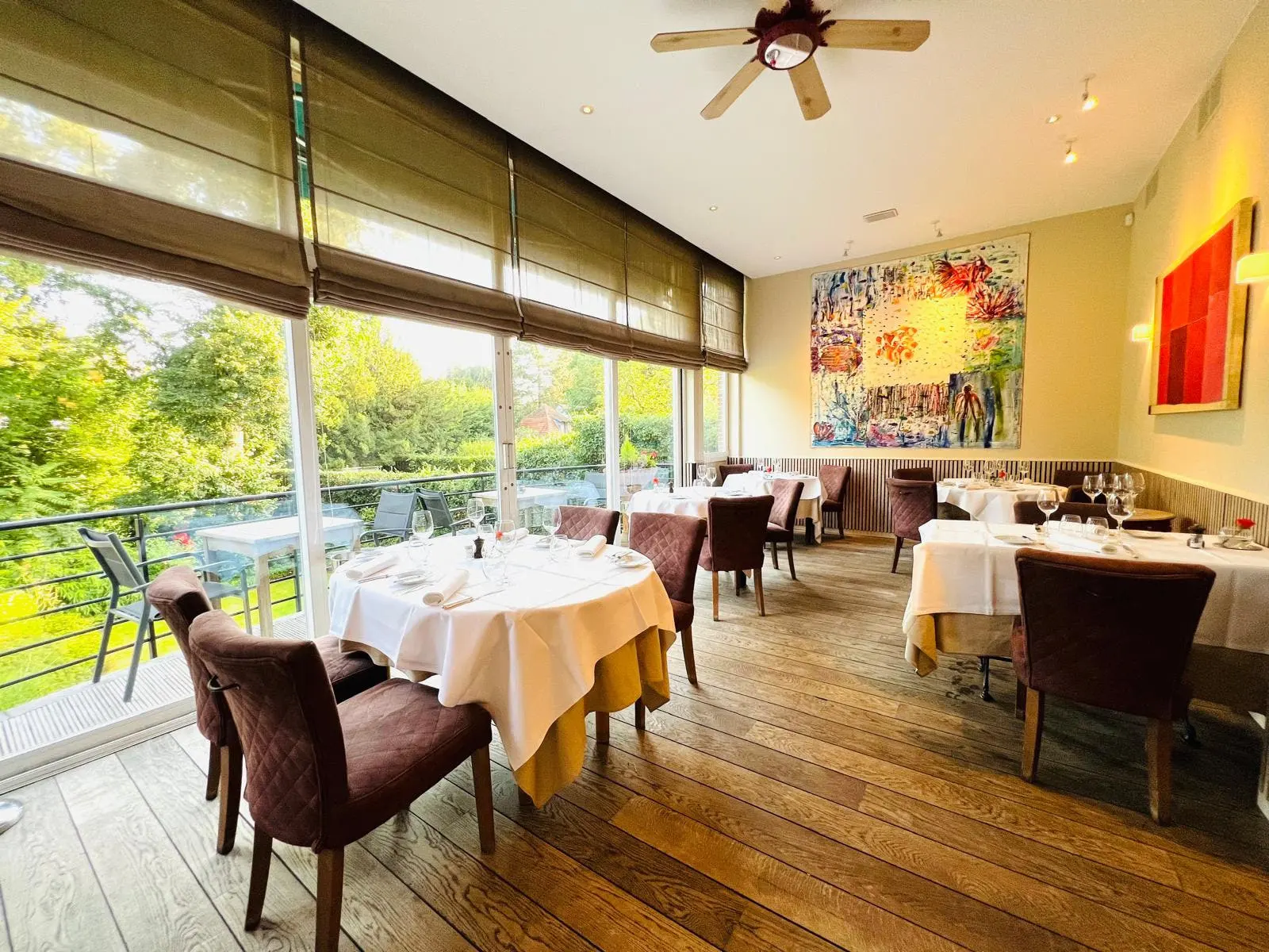 La salle du restaurant, tables dressées face à la baie vitrée sur le jardin
